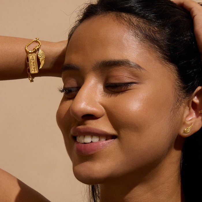 Gold-toned bracelet with rectangular wing charm pendant worn on wrist, shown on model.
