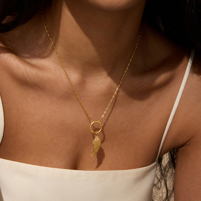 Gold-toned angel wing charm pendant on delicate chain, worn as necklace.