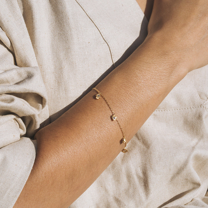Delicate gold-tone bracelet with small white topaz charms spaced along the chain, worn on wrist.