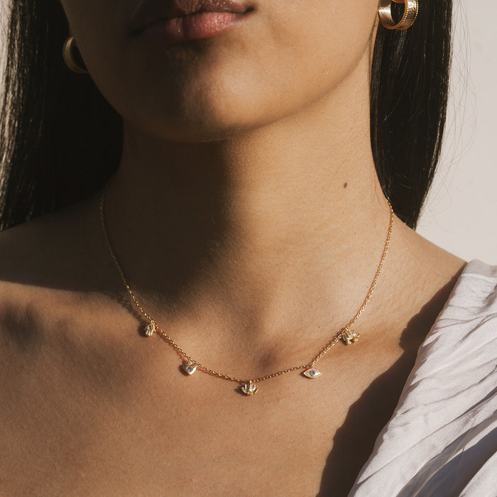 Gold-toned choker necklace with white topaz charms featuring symbolic designs, worn close to the neck.