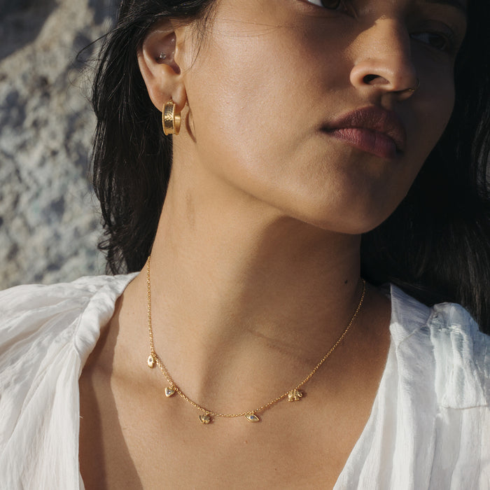 Gold-toned choker necklace with small crystal charms spaced along a delicate chain, worn close to the neck.