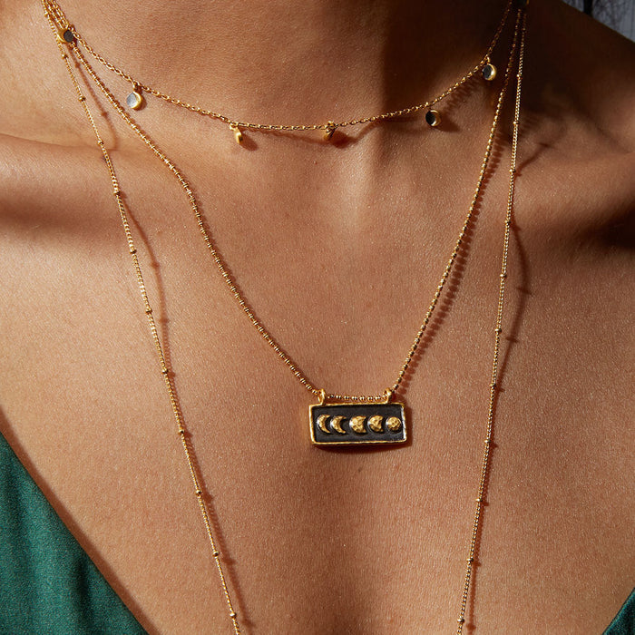 Close-up of the Self Evolution Moon Phase Necklace worn layered with delicate gold chains, illustrating its role as a meaningful talisman for spiritual and yoga practices, embodying the essence of the sun and moon.