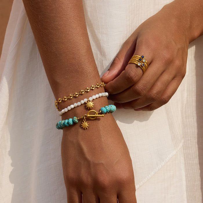 White howlite beaded bracelet with gold-tone toggle clasp and sun charm, worn on wrist.
