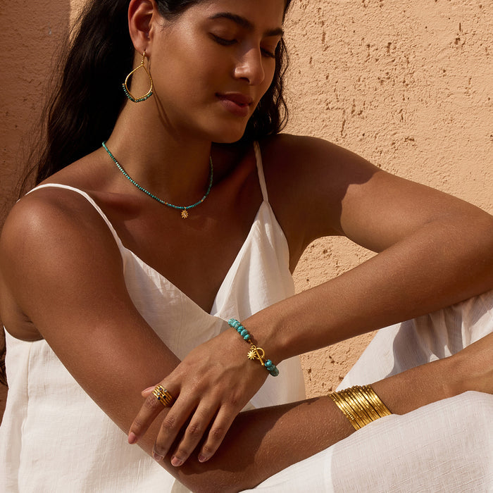 White and teal beaded bracelet with gold toggle clasp worn on wrist.