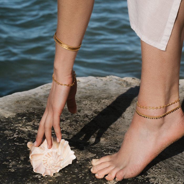 Gold-toned chain anklet worn on ankle with small coin-shaped charms.