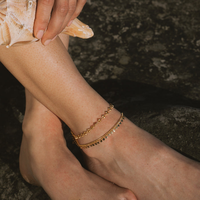 Gold chain anklet with small coin charms worn on ankle.
