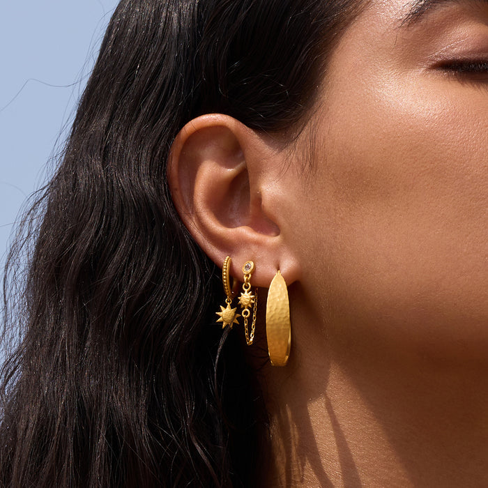 Gold-toned hoop earrings with hammered texture worn on ear, including chain-link design with star charm.
