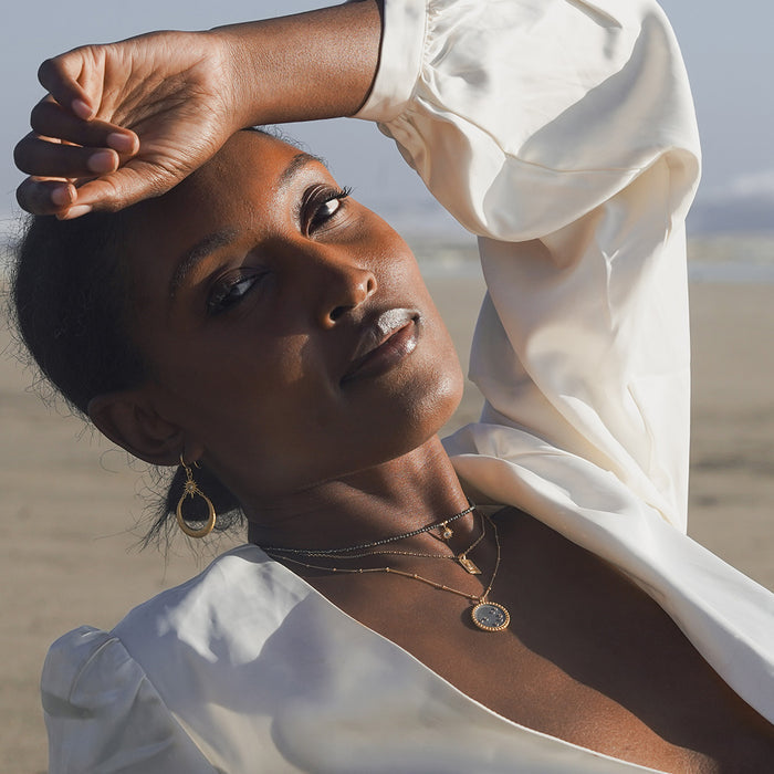 A model wearing the Shine in Sisterhood Constellation Necklace on a beach, exuding confidence and spirituality. This necklace, with its powerful symbolism of the sun and moon, serves as a protective talisman in your spiritual journey, enhancing your yoga practice and meditation.