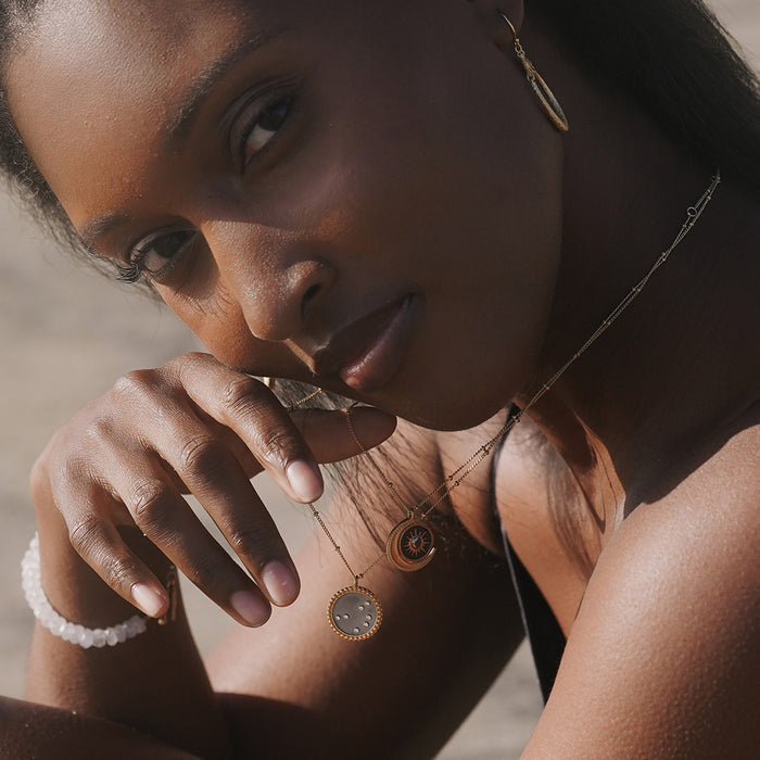 A close-up shot of a woman elegantly showcasing the Shine in Sisterhood Constellation Necklace, which symbolizes spiritual connection and empowerment. The necklace features a gold-plated pendant adorned with seven pyrite stars, representing reflection and prosperity. This piece of spiritual jewelry is perfect for those who embrace meditation and seek meaningful talismans for protection and manifestation, complementing practices like yoga and connecting with the energies of the sun and moon.