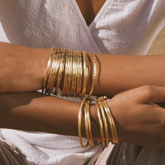 Gold-toned bangle bracelets stacked on wrists, worn with a light pink cardigan.