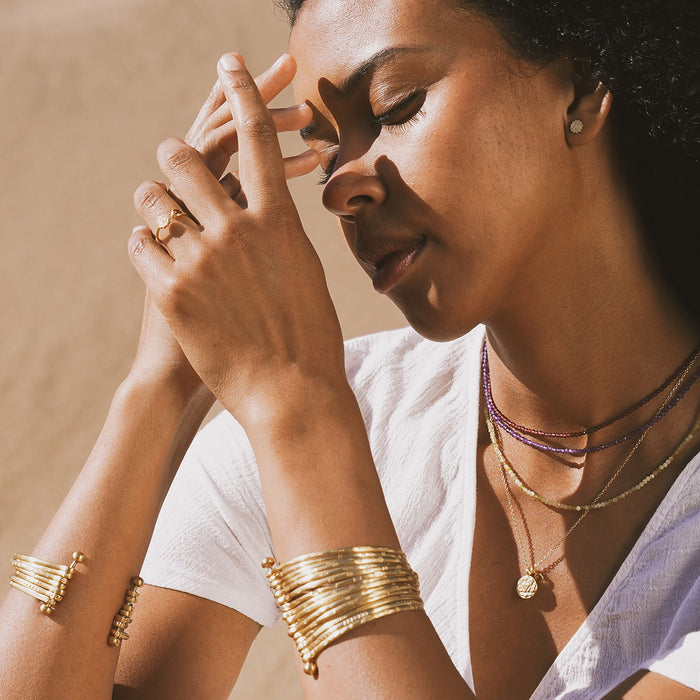 Gold bangle bracelet cuff worn on wrist, shown with matching gold rings and necklaces.