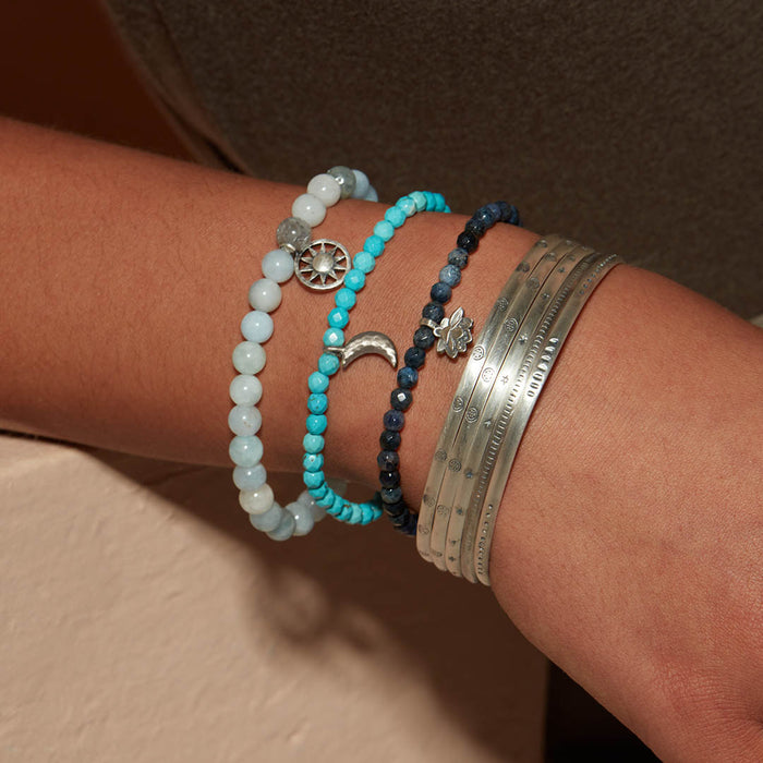 A wrist adorned with the Small Silver Multi Bangle Cuff alongside various beads, reflecting a blend of styles that resonates with spiritual jewelry themes. These pieces serve as meaningful reminders for meditation and yoga, offering manifestation and protection.