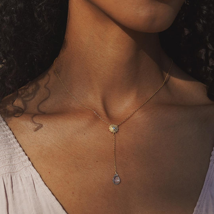 A model wearing the Speak with Strength Chakra Lariat Necklace with a soothing expression, showcasing the beautiful blue topaz drop as a talisman for positive energy, perfect for spiritual and yoga practices.
