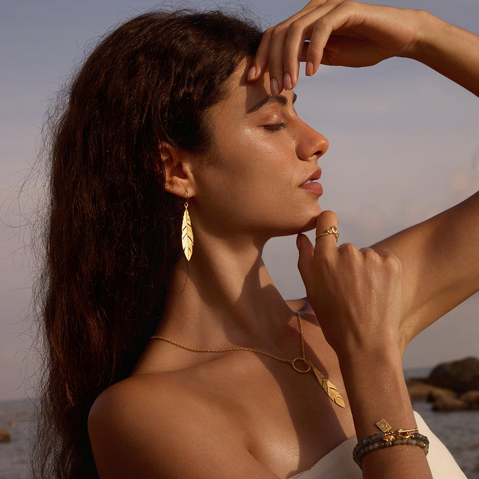 A model gracefully wearing the Spiritual Messenger Feather Earrings, emphasizing their elegance and spiritual significance. These earrings serve as a meaningful accessory for meditation, embodying the themes of sun and moon, and connect to the essence of yoga and personal manifestation.