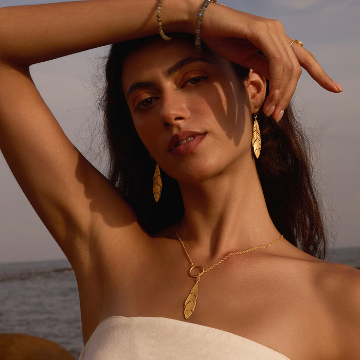 A woman poses wearing Spiritual Messenger Feather Earrings, beautifully capturing the essence of spiritual jewelry. The delicate feather design symbolizes a connection to the spiritual realm, making it a meaningful talisman for meditation and protection. Perfect for yoga enthusiasts and those interested in zodiac and manifestation, these earrings shine under the sun and moon, enhancing their significance in daily life.