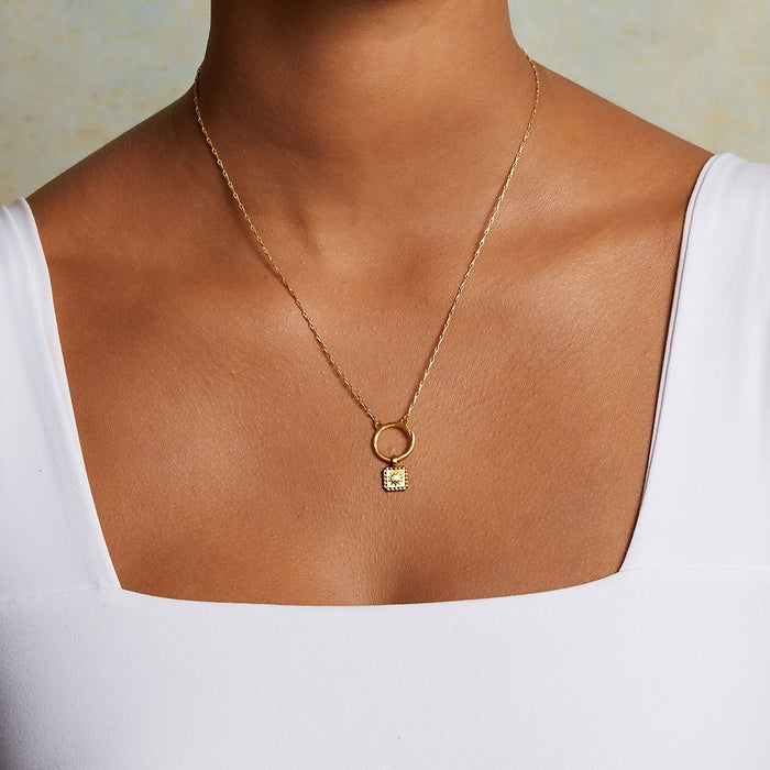 Model wears the Sun Square Charm necklace, an 18kt gold plated charm symbolizing vitality and leadership, perfect for spiritual jewelry and meaningful meditation practice. This talisman complements the themes of zodiac, malas, and yoga, enhancing protection and manifestation.