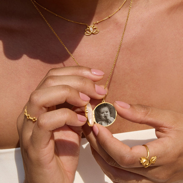 Gold-toned butterfly pearl locket necklace with oval pendant containing a sepia photograph, worn on gold chain.