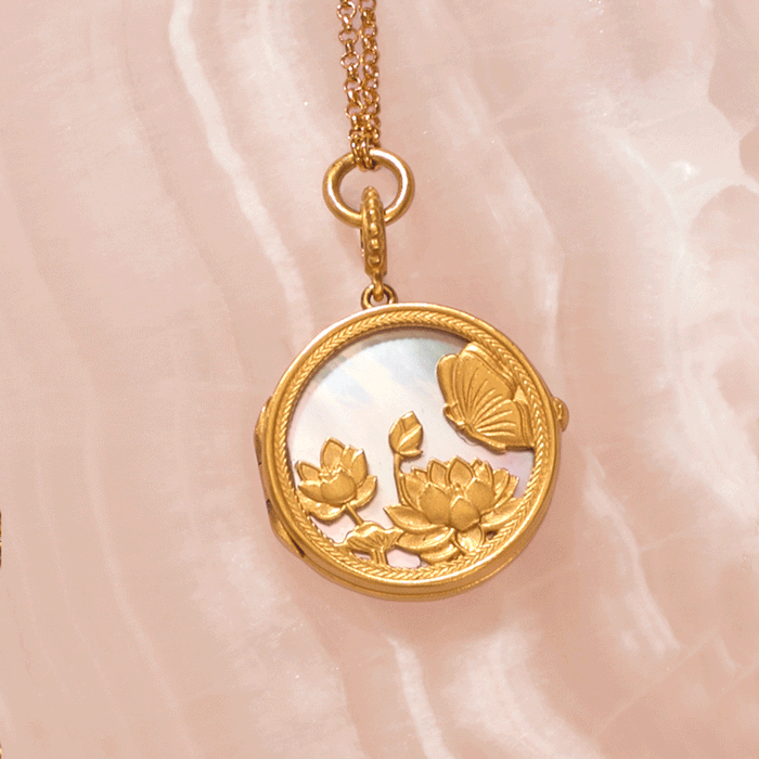 Gold-toned circular locket pendant with mother-of-pearl center, featuring embossed lotus flowers and butterfly, hanging from