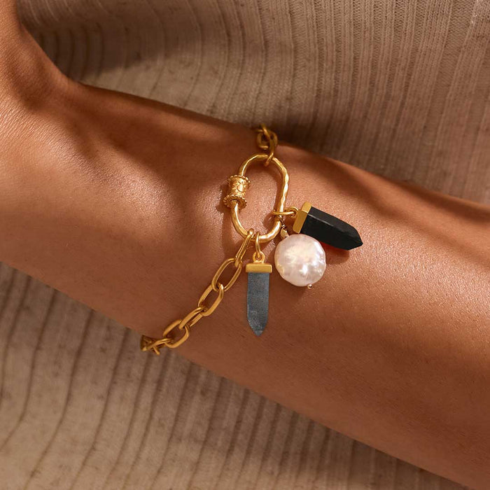 Gold-toned charm bracelet with white pearl, black stone, and gray crystal pendant charms worn on wrist.