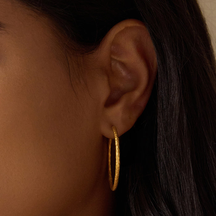 Close-up of a person wearing Textured Gold Large Hoop Earrings, showcasing the elegant design perfect for minimalist style. These earrings symbolize spiritual jewelry, embodying meaning and manifestation, ideal for yoga practice and meditation.