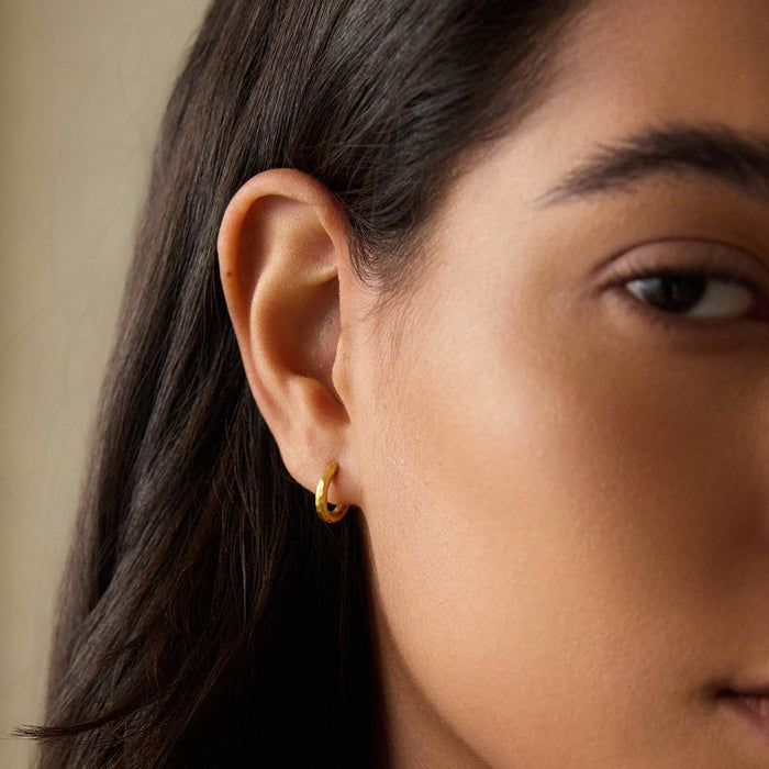 Close-up of Textured Gold Mini Hoop Earrings worn on an ear, illustrating their minimalist impact as spiritual jewelry ideal for enhancing your style during yoga or meditation sessions, connected with meaningful symbolism.