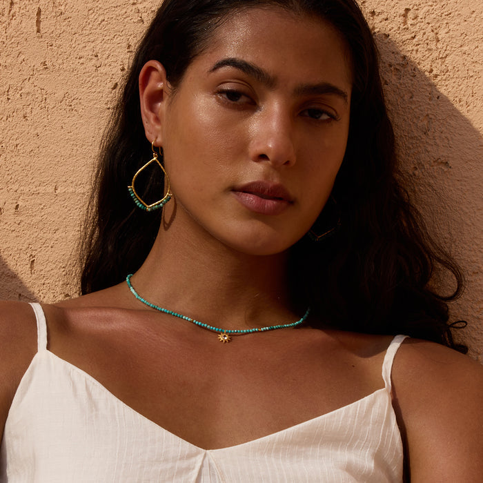 Turquoise beaded choker necklace with gold sun pendant, worn with matching beaded hoop earrings.