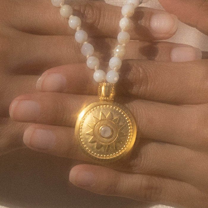 A detailed view of the sun pendant on the Tranquil Dawn White Opal Sun Mala, with white opal beads surrounding it, representing protection and spiritual meaning in yoga and meditation.