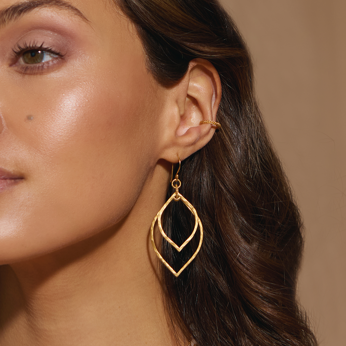 Close-up of a model wearing the Transformed by Light Lotus Linear Earrings, highlighting their shimmering gold design. This spiritual jewelry piece serves as a beautiful talisman for protection and embodies qualities of the sun and moon, enhancing yoga and meditation rituals.