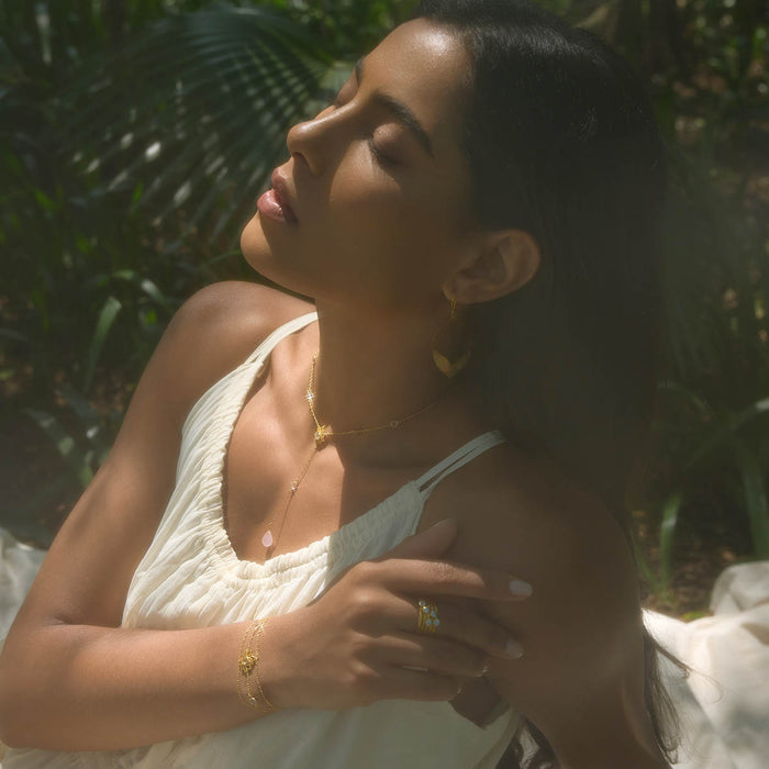 Close-up of a model wearing the Transformed by Love Lotus Bracelet in a serene outdoor setting, highlighting its spiritual significance. The bracelet, made with rose quartz, serves as a meaningful accessory for yoga and meditation, representing protection and the energy of the sun and moon.