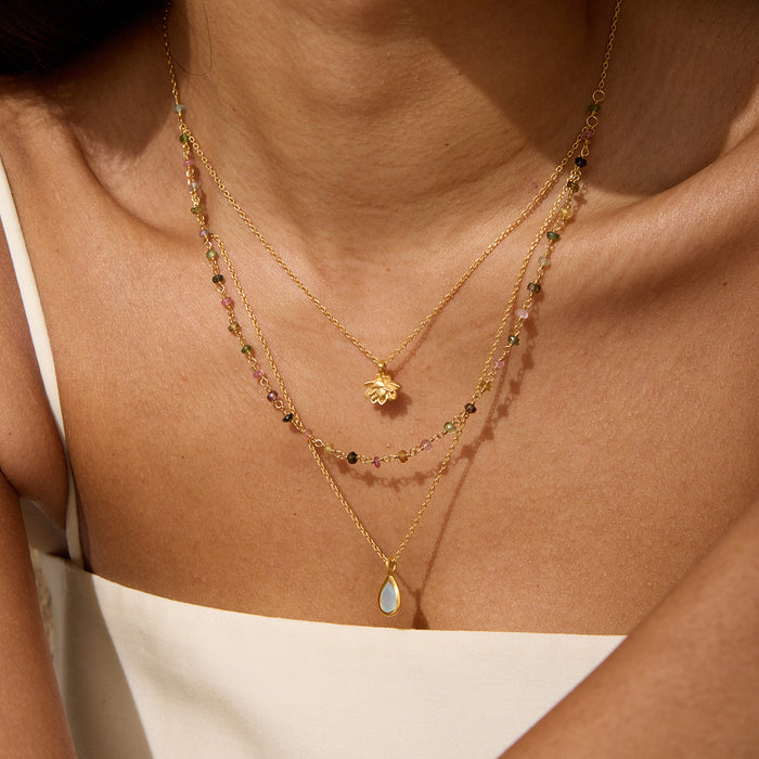Three-strand gold necklace with lotus flower pendant, tourmaline agate beads, and teardrop stone pendant worn layered on ches