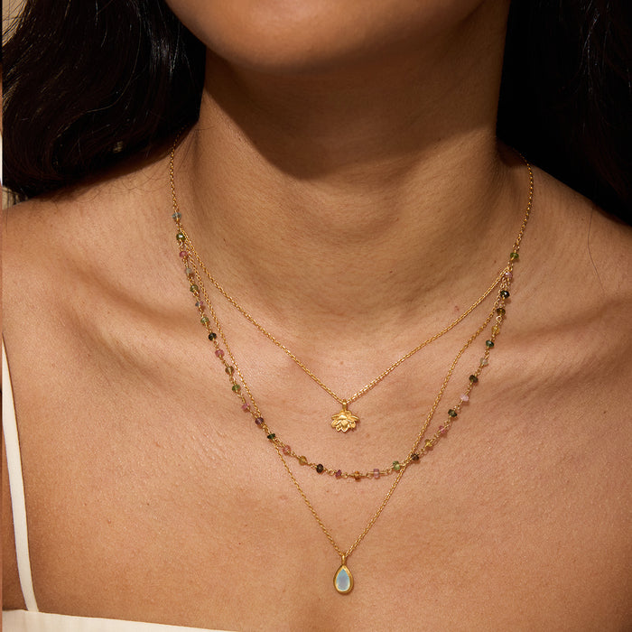 Gold layered necklace with three strands featuring beaded tourmaline, lotus charm pendant, and teardrop agate stone.