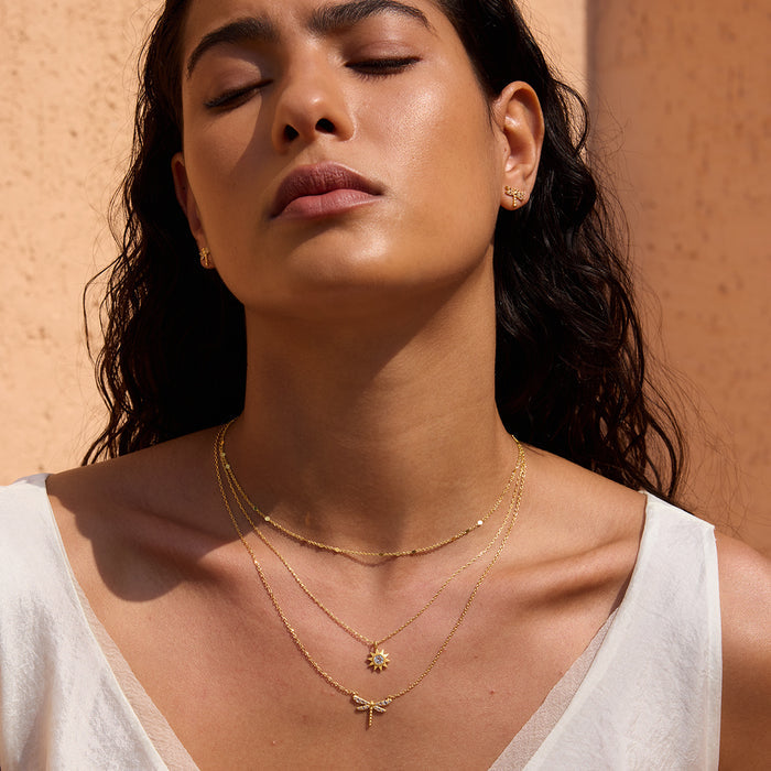 Gold dragonfly stud earrings with white topaz stones worn on model's ears.