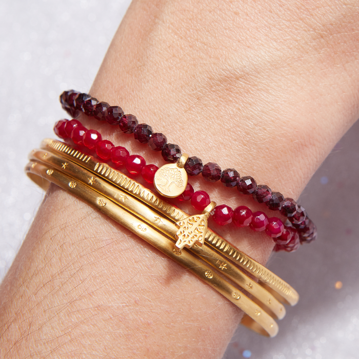 Tree of Life Garnet Gemstone Bracelet worn on a wrist alongside other golden bangles. This stylish piece represents meaningful spirituality, ideal as a yoga accessory that embodies protection and sacred symbolism.