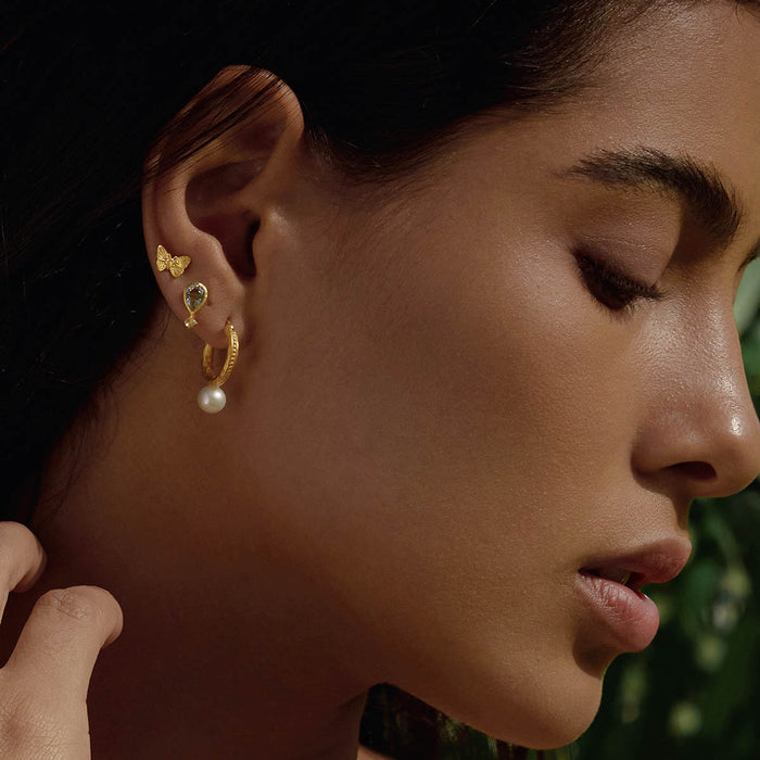 Close-up of a woman wearing True Self Green Amethyst Earrings along with other delicate jewelry pieces. The green amethyst and rose quartz earrings reflect the essence of spirituality and personal meaning, making it a great talisman for zodiac lovers and those on a journey of self-discovery and protection.
