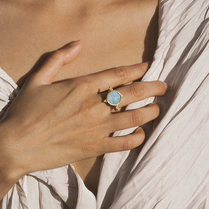 Gold-toned spinner ring with pale blue labradorite stone center worn on model's hand.