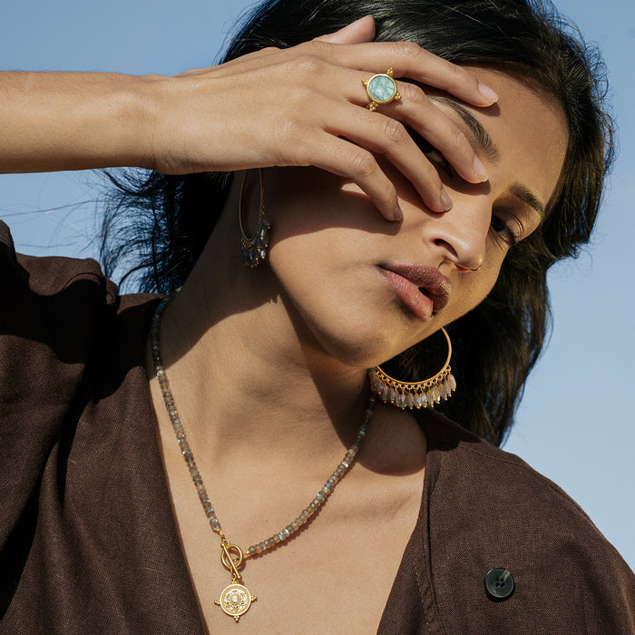 Gold-toned spinner ring with iridescent labradorite stone in lotus design, worn on hand.
