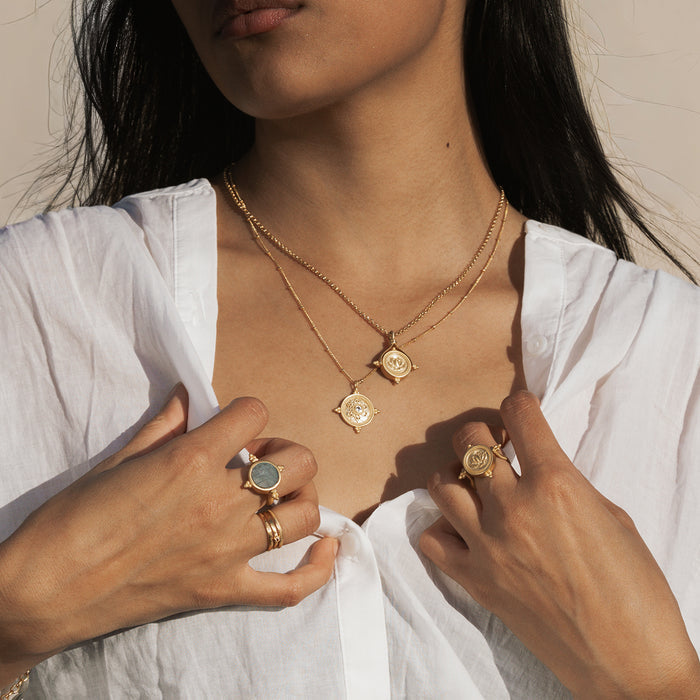 Gold spinner ring with gray-green labradorite stone center, worn on hand with matching pendant necklaces.
