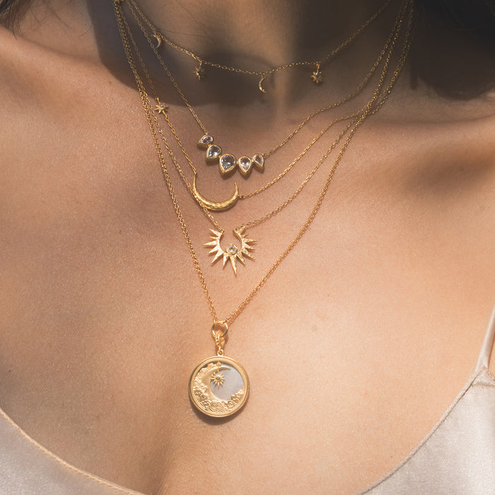 Waking Dreams Mother of Pearl Celestial Necklace featured in a layered jewelry look, accenting the spiritual journey of the wearer. This gold pendant showcases the celestial harmony of the sun, moon, and stars, ideal for meditation, manifestation, and meaningful protection.