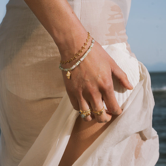 Gold chain bracelet with white beads and small gold charm pendant worn on wrist.