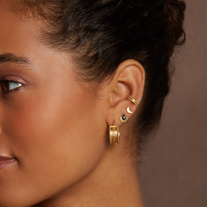 A profile image of a woman showcasing Whimsical Spirit White Topaz Bold Hoop Earrings alongside other gold jewelry. This spiritual piece embodies protection and manifestation, adding charm to any zodiac-inspired collection.