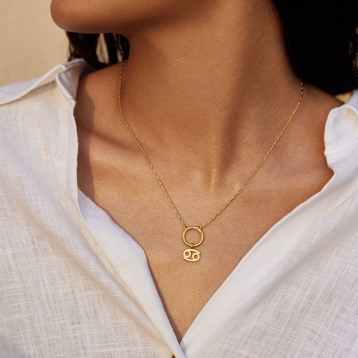A woman wearing a Zodiac Glyph Charm Cancer pendant on a delicate gold chain. This spiritual jewelry piece symbolizes the protective qualities of the Cancer zodiac, making it a great talisman for meditation and meaningful expressions.